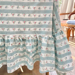 A close-up of a aqua striped hand block printed tablecloth with floral patterns and a ruffled border on a table.