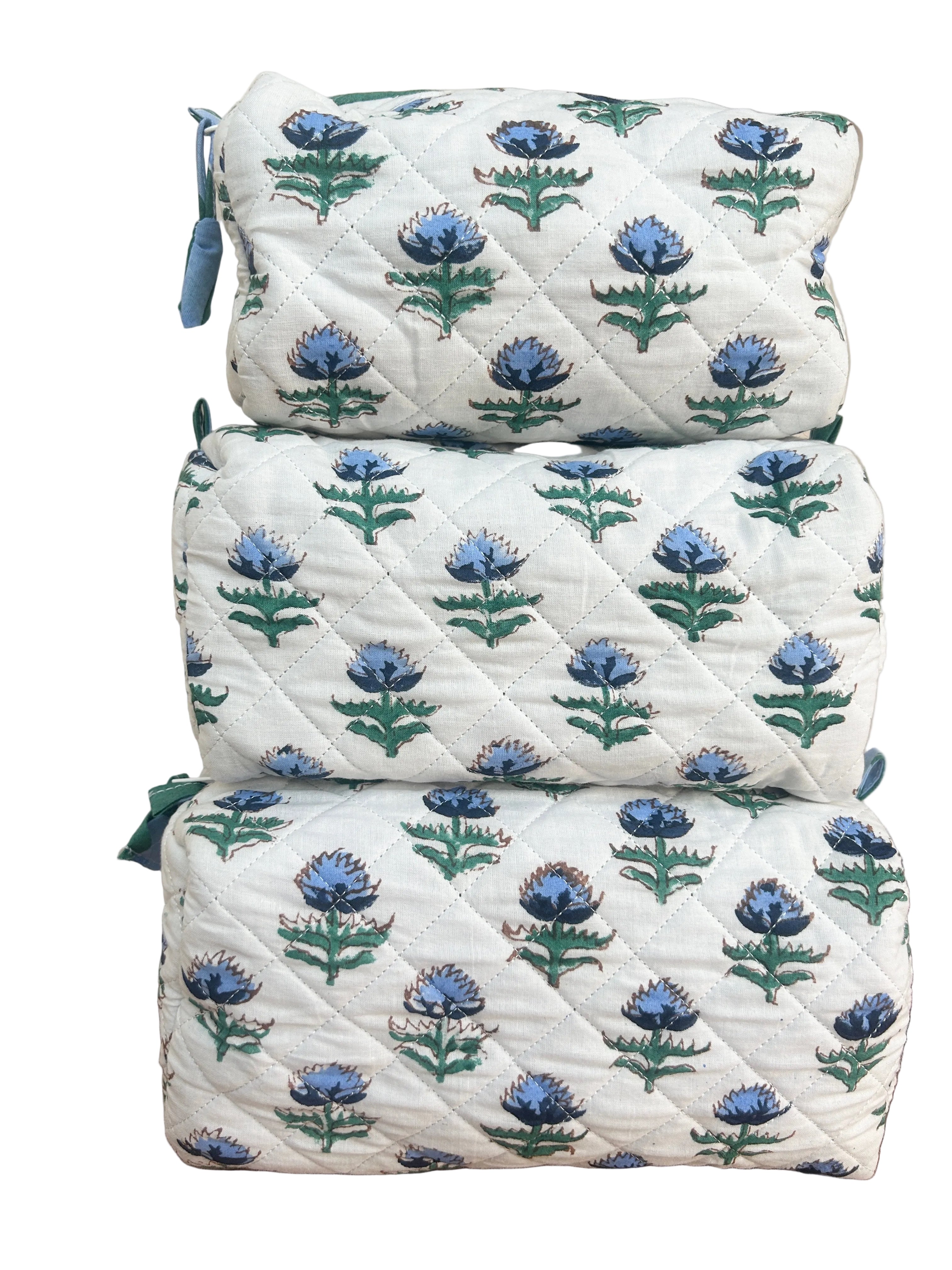 Set of three floral-patterned quilted wash bags stacked on a wooden surface. The Charpoy