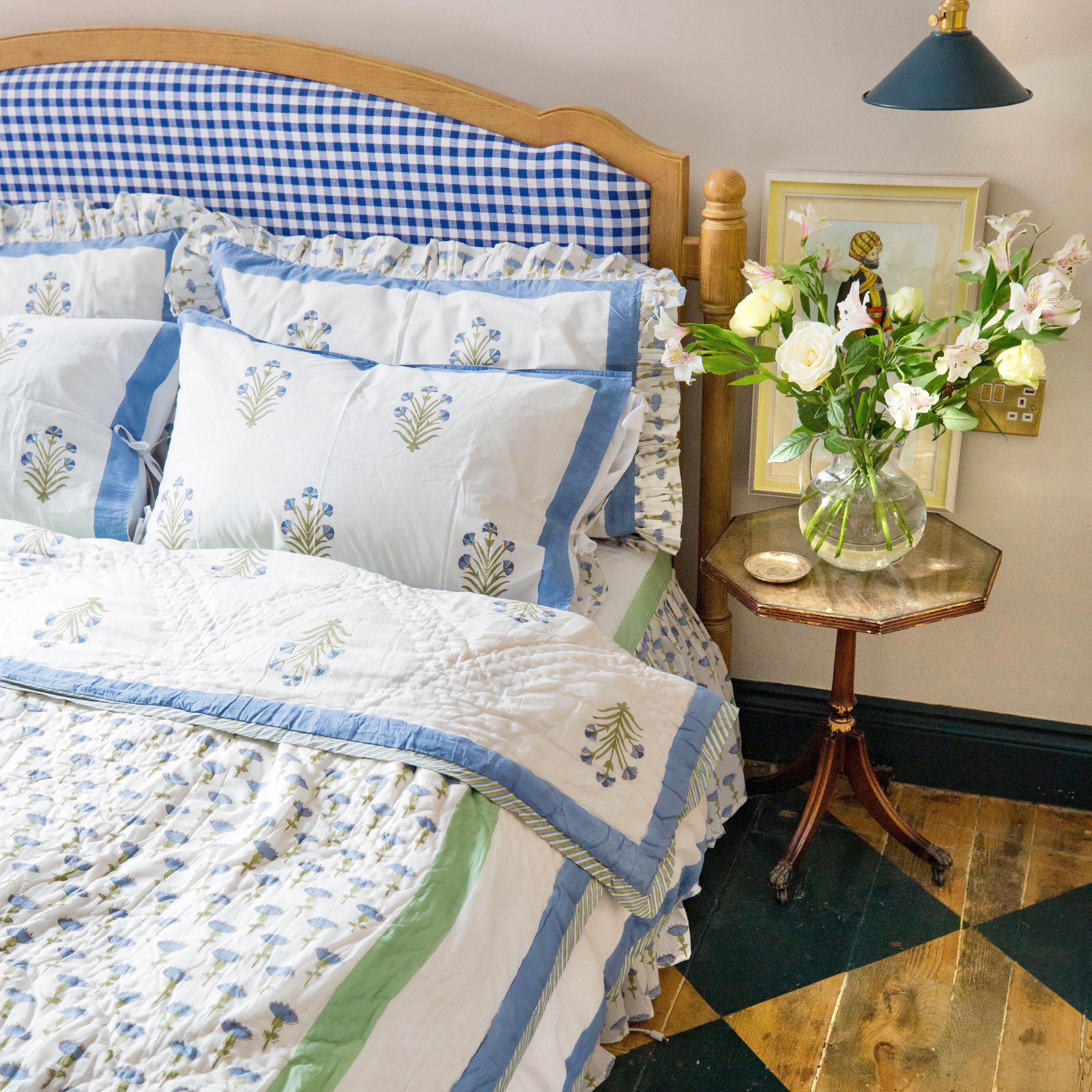 A bedroom setting with the reverse of the Blue Carnation quilt draped on a bed, featuring floral block print designs, muslin cotton fabric, handmade by artisans in Jaipur for The Charpoy