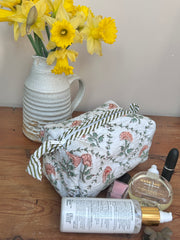 Floral-patterned bag with skincare products and a vase of yellow flowers on a wooden surface The Charpoy