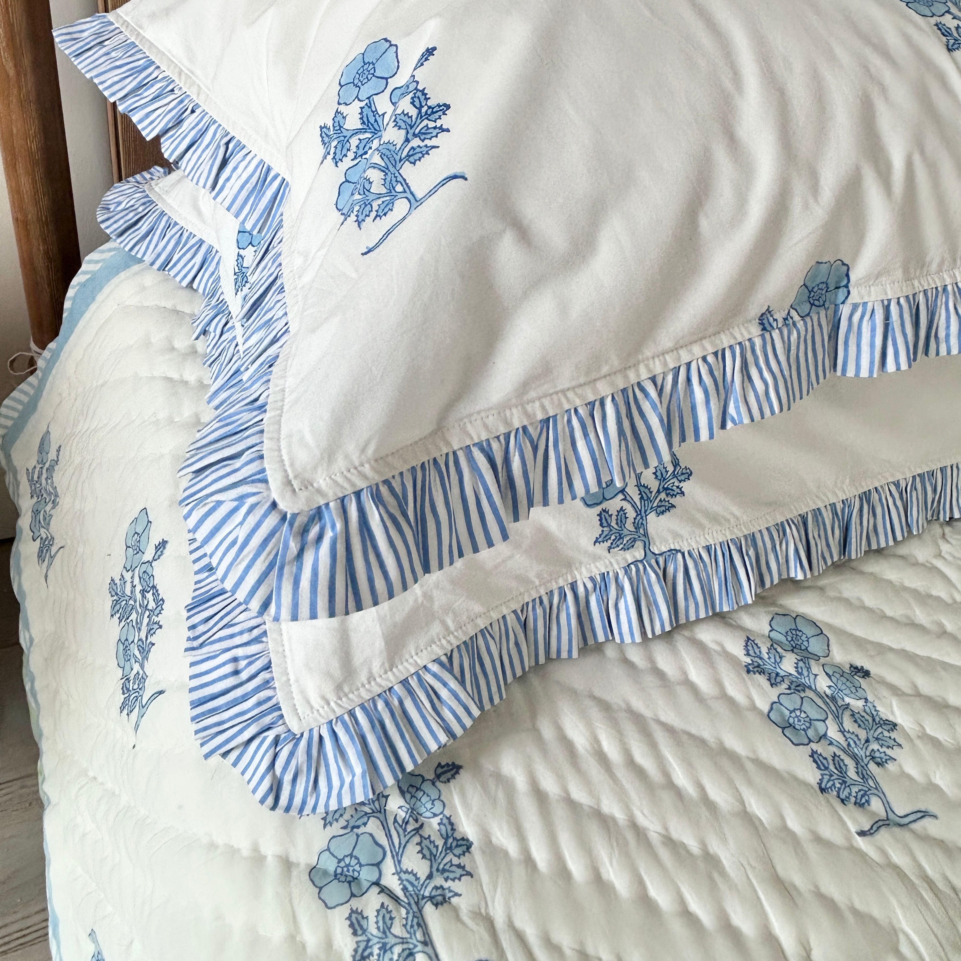Jodhpur Blue Floral Hand Block Printed Quilt on a bed with matching ruffled pillows, artisanal made in Jaipur by The Charpoy