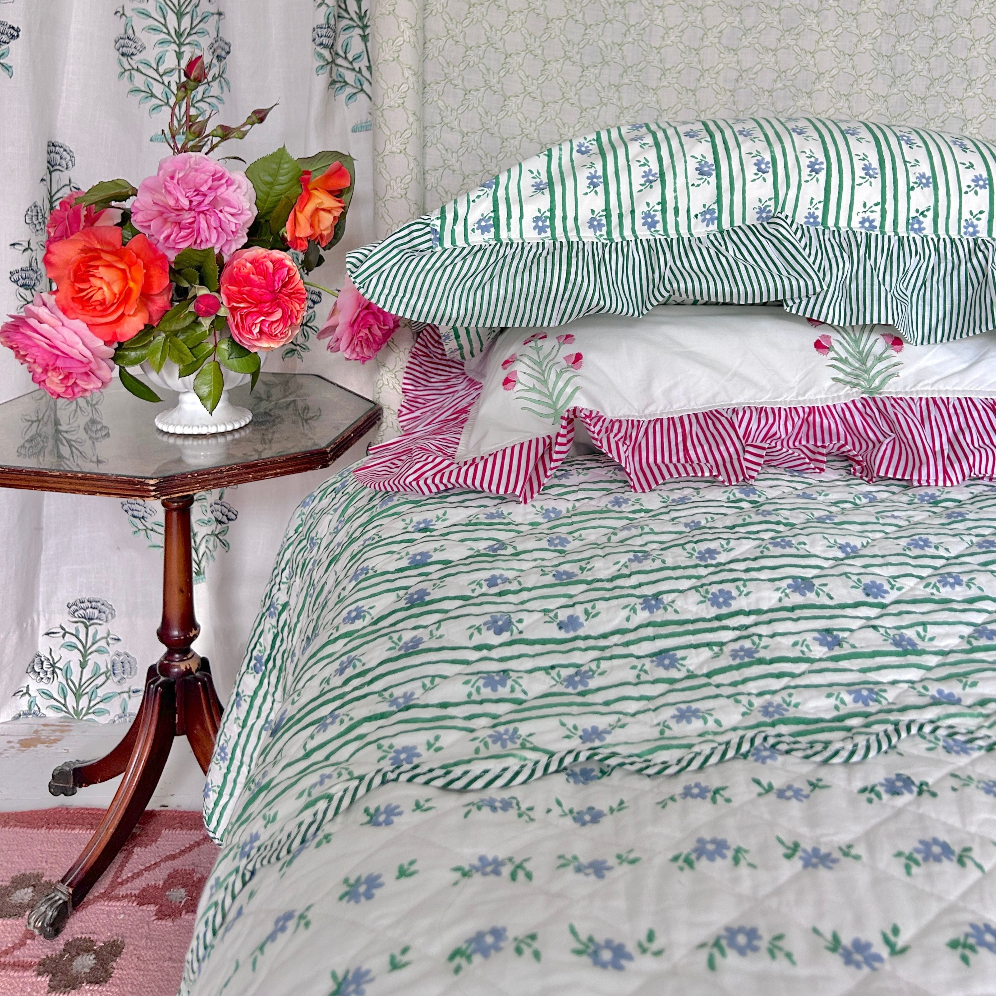 Striped hand block printed bedspread, with pillow covers and flowers on a wooden table. The Charpoy