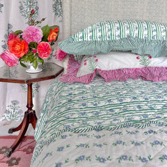 Striped hand block printed bedspread, with pillow covers and flowers on a wooden table. The Charpoy