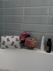 Bathroom setting of a Pink And Green Flower Quilted Wash Bag hand block printed and lightly quilted by artisans in Jaipur by The Charpoy with flowers, and toiletries against a tiled wall.