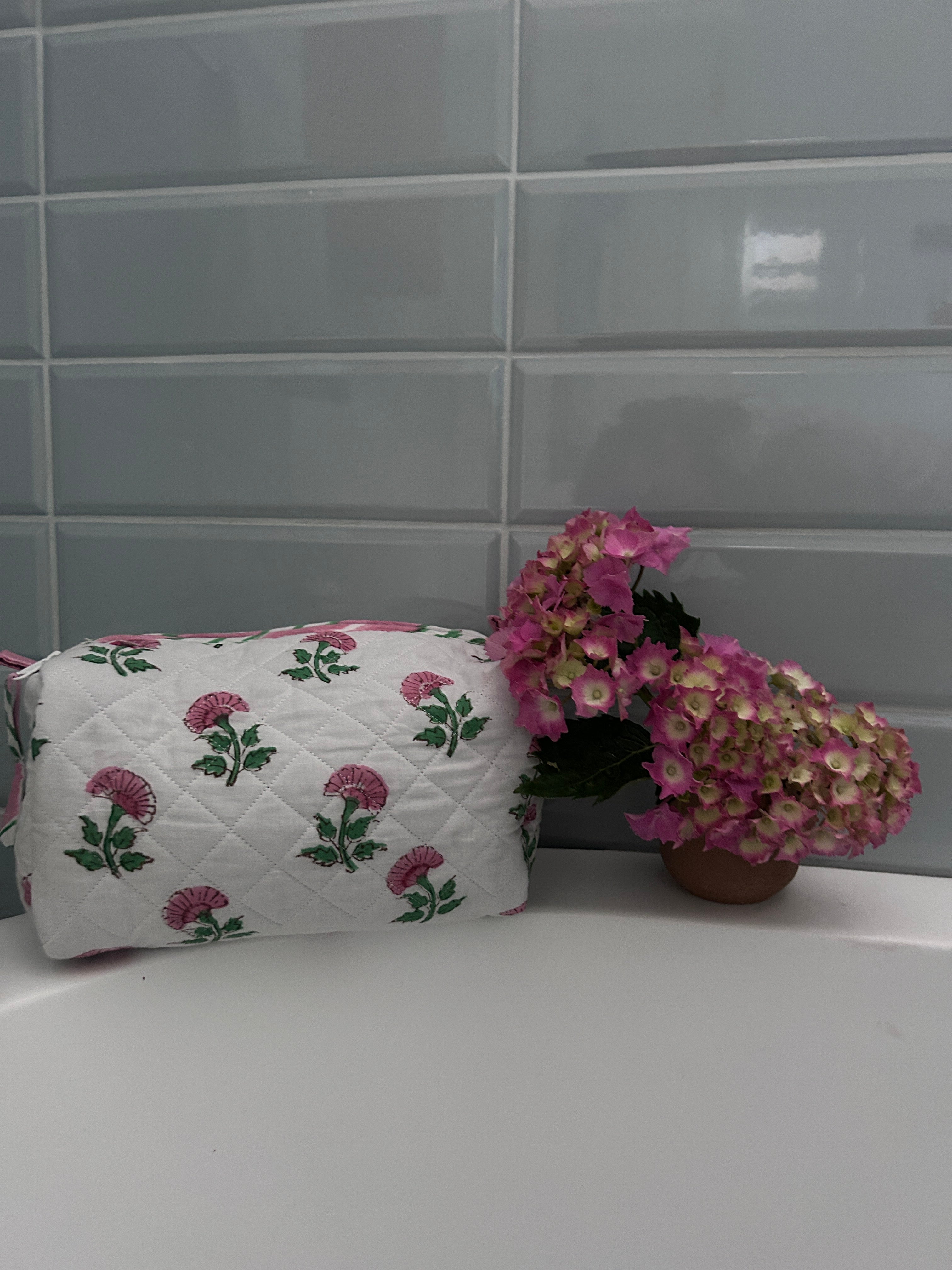 Pink And Green Flower Quilted Wash Bag hand block printed and lightly quilted by artisans in Jaipur by The Charpoy on a bath tub in a bathroom setting.