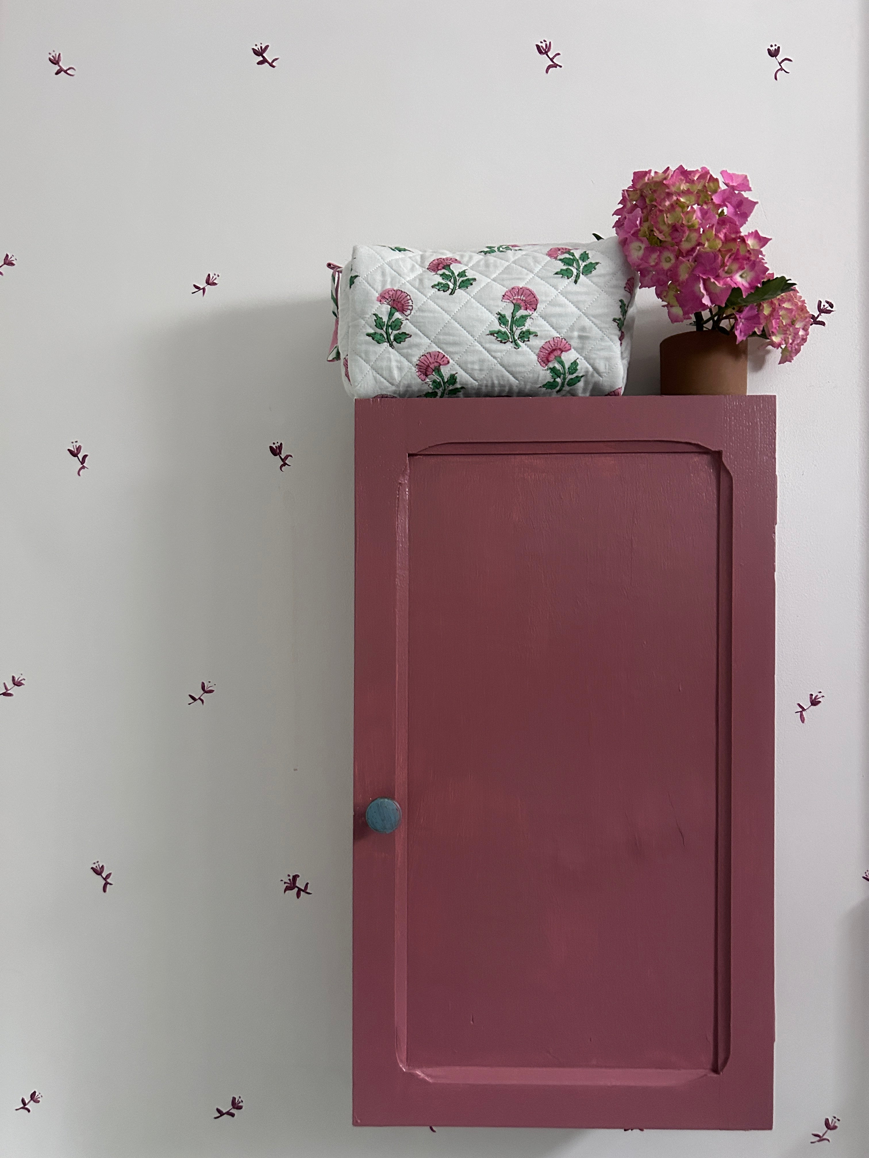 Pink And Green Flower Quilted Wash Bag hand block printed and lightly quilted by artisans in Jaipur by The Charpoy on a Pink cabinet and floral wall in a bathroom setting.