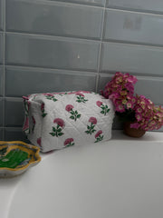 Pink And Green Flower Quilted Wash Bag hand block printed and lightly quilted by artisans in Jaipur by The Charpoy on a bathtub against a tiled wall in bathroom setting.