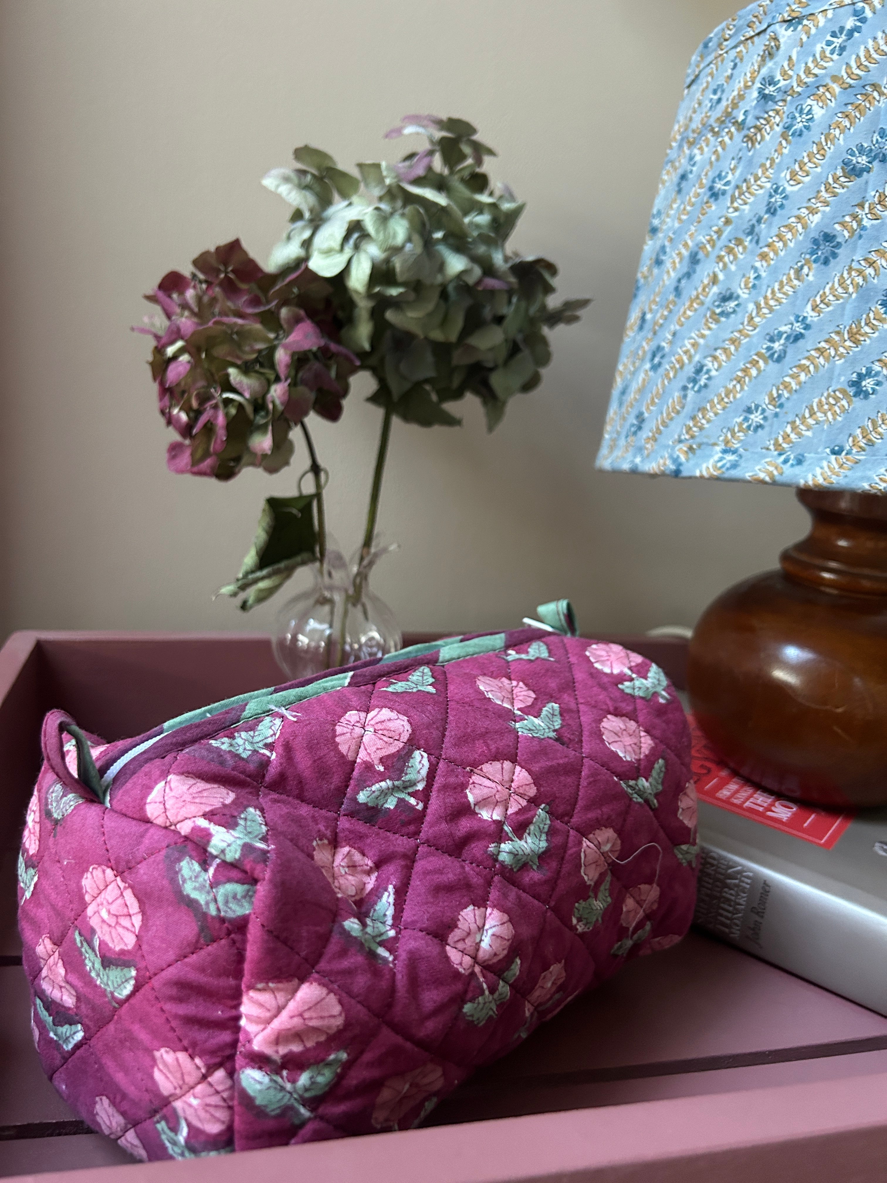 Floral-patterned wash bag on a chair next to a plant and decorative items. The Charpoy