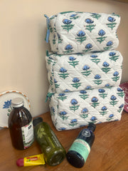Stack of floral-patterned quilted Wash bags with various bottles on a wooden surface. The Charpoy 
