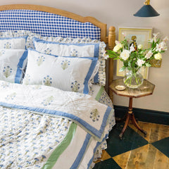 A bedroom setting with the reverse of the Blue Carnation quilt draped on a bed, featuring floral block print designs, muslin cotton fabric, handmade by artisans in Jaipur for The Charpoy