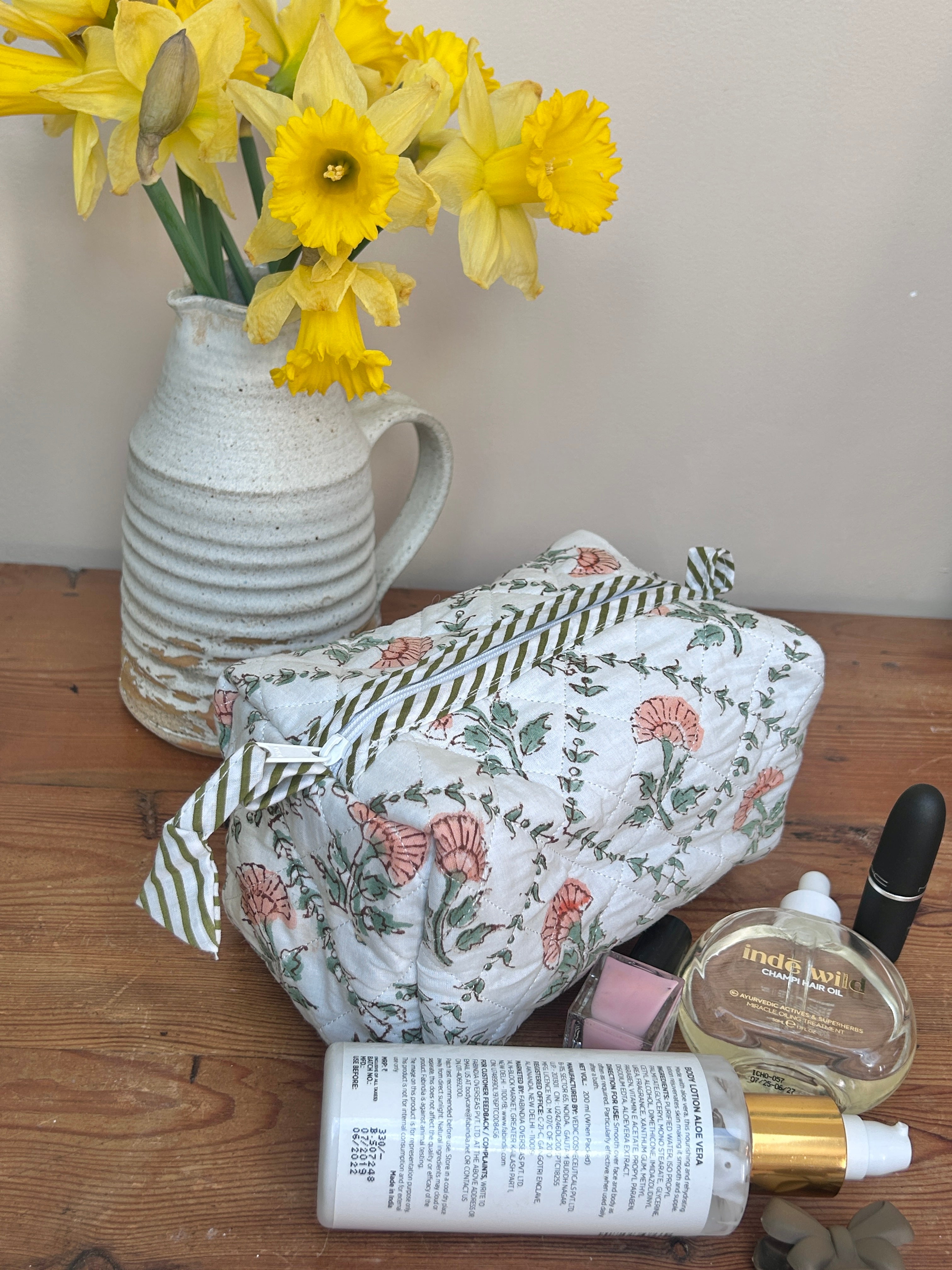 Floral-patterned bag with skincare products and a vase of yellow flowers on a wooden surface The Charpoy