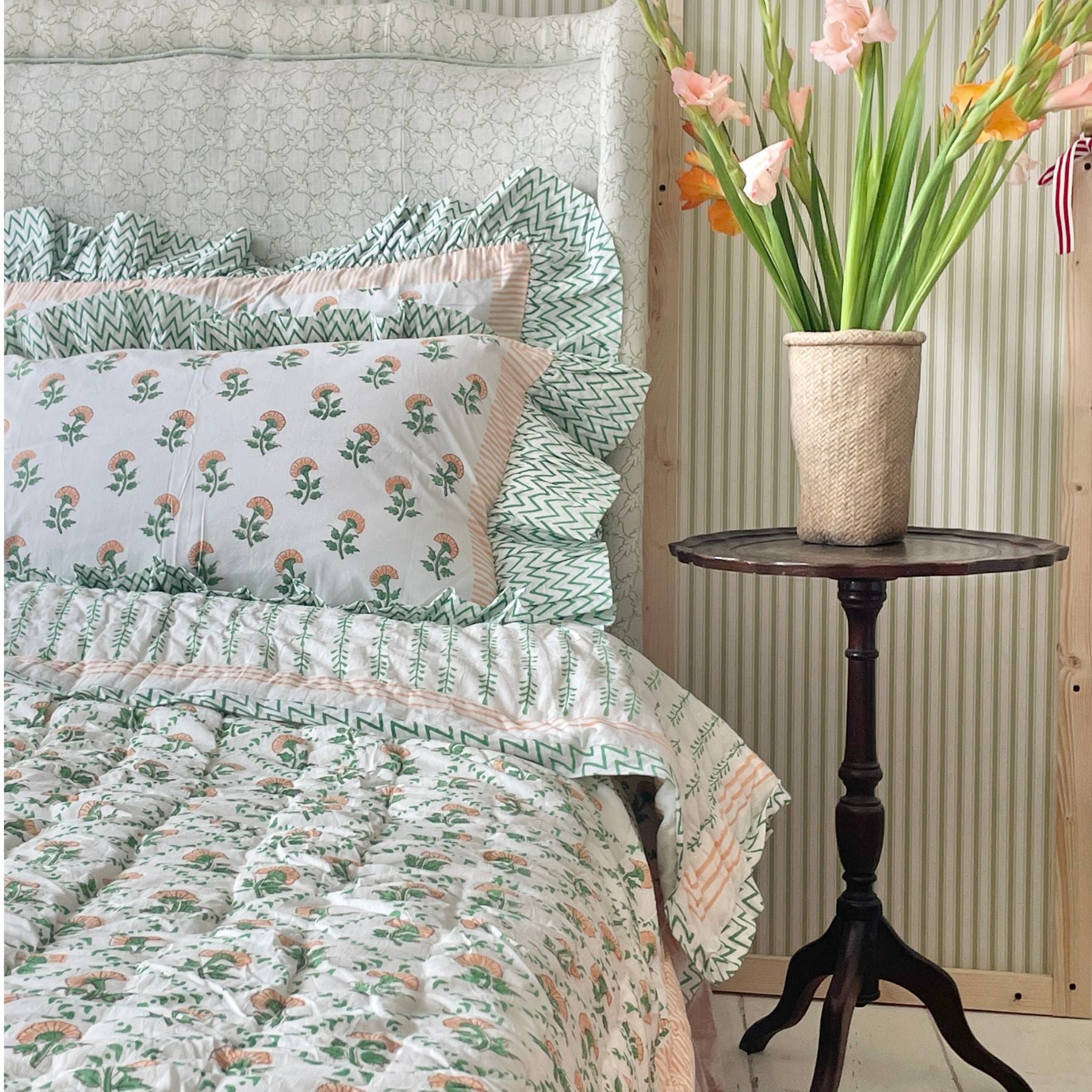 A peach flower hand block printed quilt with a botanical motif displayed on a bed. by The Charpoy