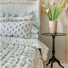 A peach flower hand block printed quilt with a botanical motif displayed on a bed. by The Charpoy