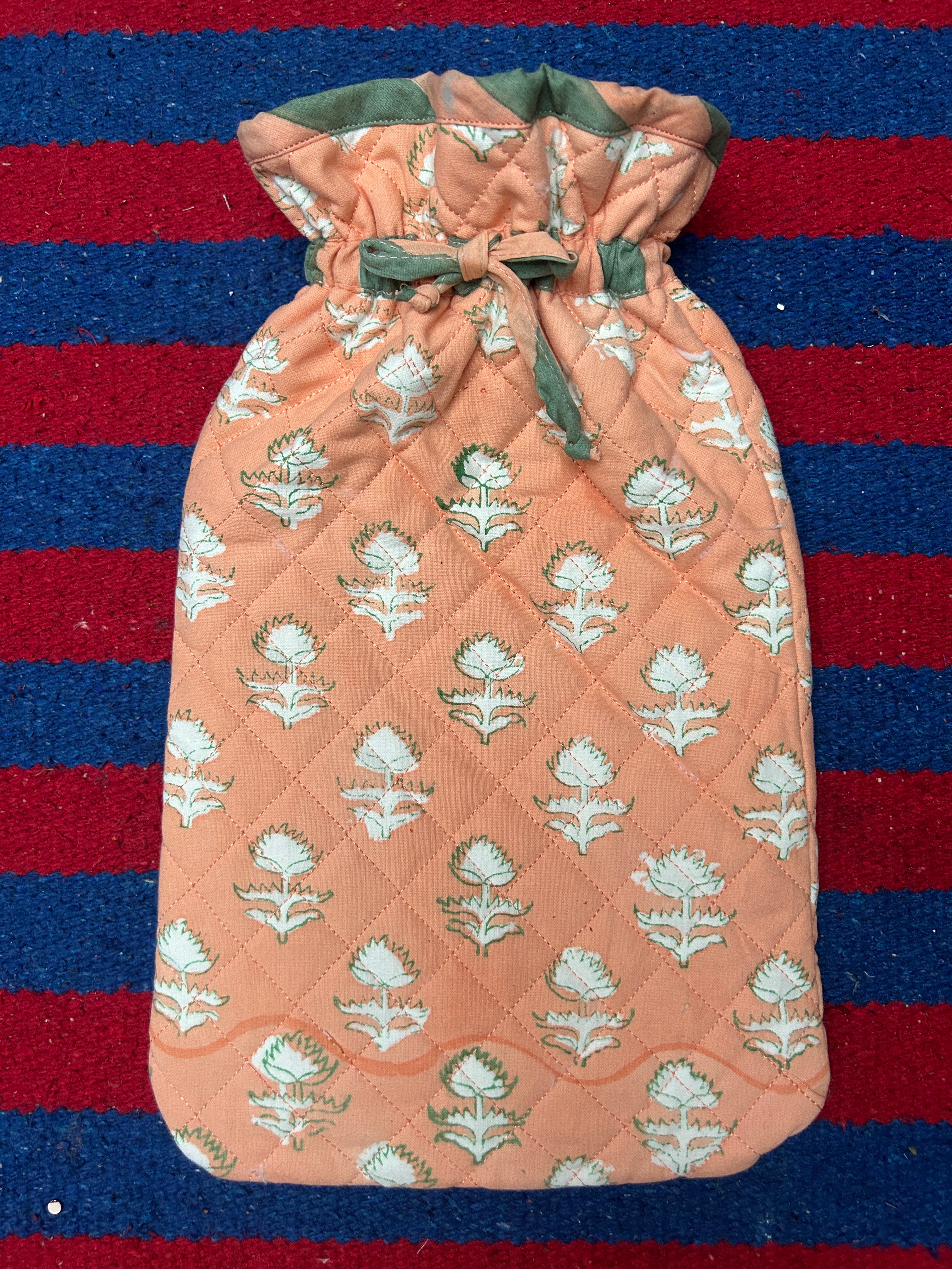 Hot water bottle cover in Quilted fabric with peach pattern on a red and blue striped background