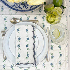 Close up of the Hand block printed white tablecloth with petit blue daisy garland motifs, embroidered scalloped edge, with matching napkins placemats styled on a dining table by The Charpoy