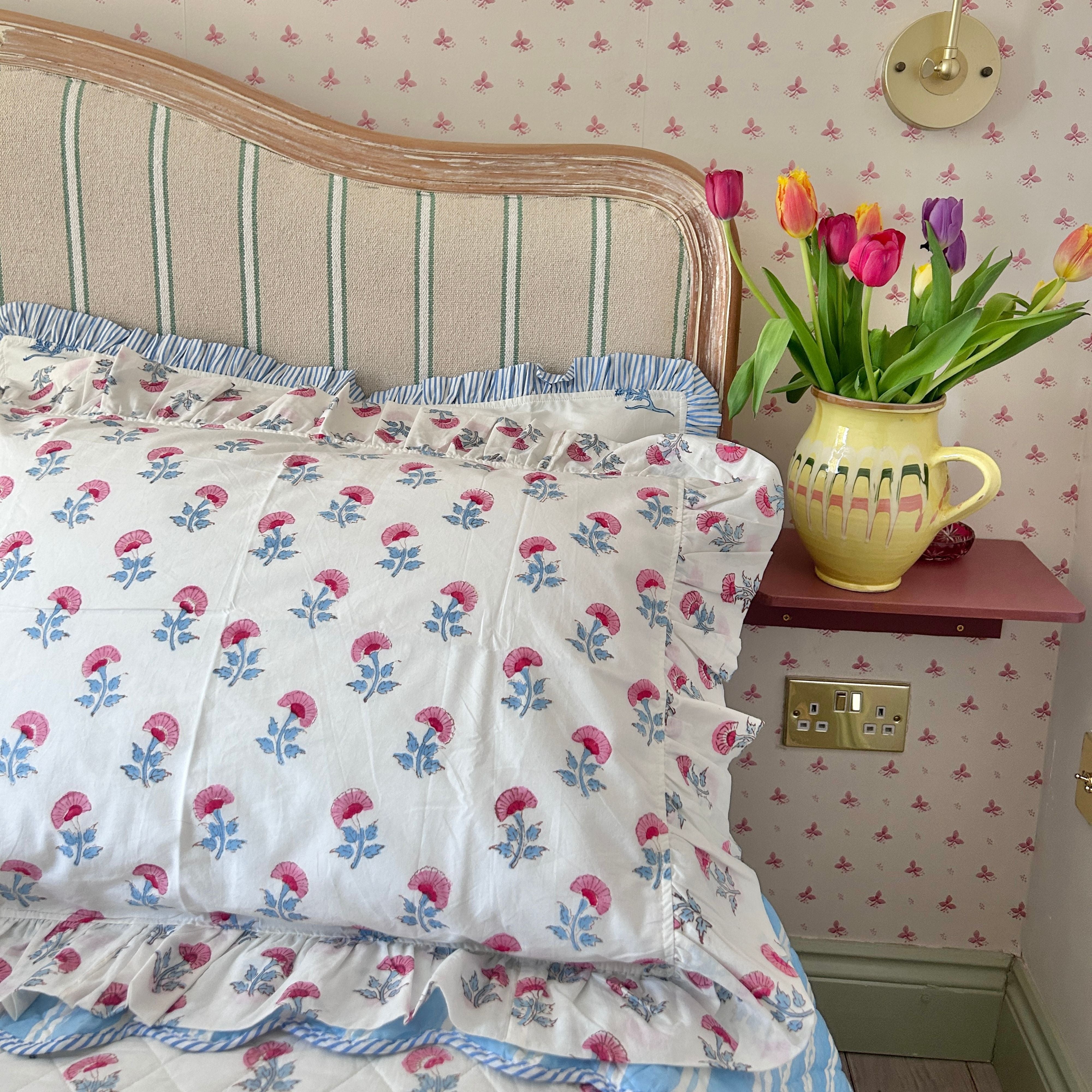 Floral hand block printed pillow covers with a vase of tulips on a shelf in a bedroom. The Charpoy