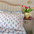 Floral hand block printed pillow covers with a vase of tulips on a shelf in a bedroom. The Charpoy