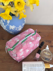 Pink floral makeup bag on a wooden surface with yellow flowers and beauty products The Charpoy