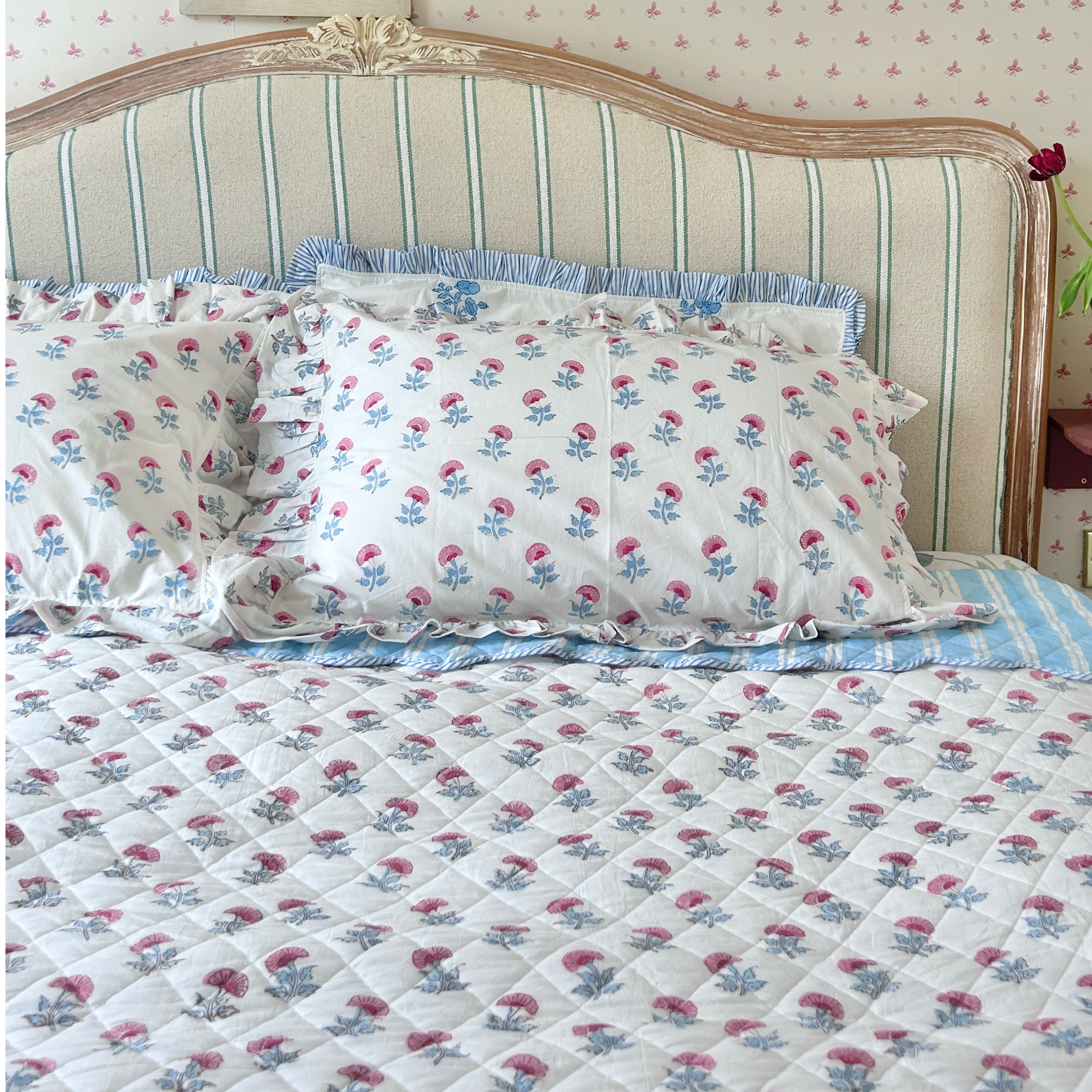Floral patterned bedspread and pillows on a bed with striped headboard. The Charpoy