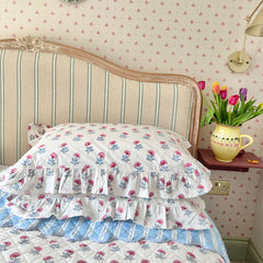 Floral hand block printed bedspread and pillows on a bed with a decorative headboard and tulips in a vase. The Charpoy
