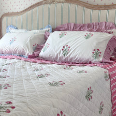 A bed dressed in pink and green buta  done with hand block printing, layered  and matched with pink flowers pillow covers set against a cream and blue striped headboard by The Charpoy