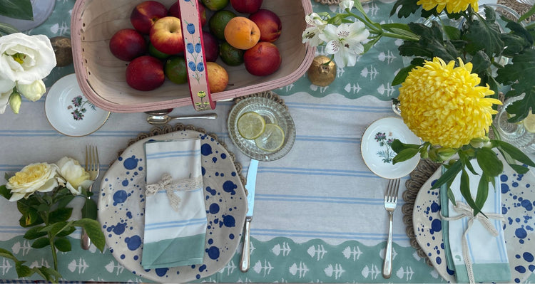 Set table with floral arrangements, fruit basket, and decorative plates on a patterned hand block printed tablecloth.